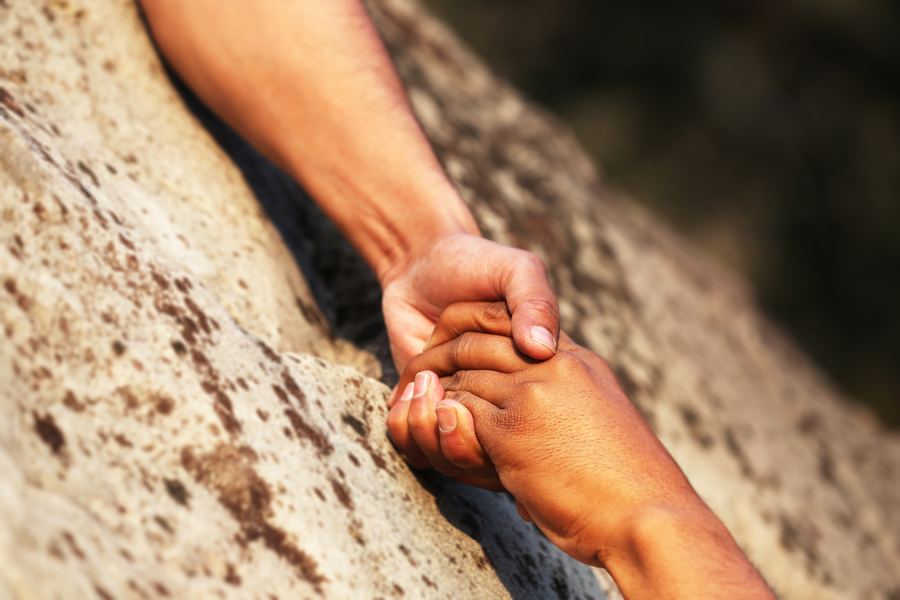 Two hands gripping each other on a rock face — trust, under load.